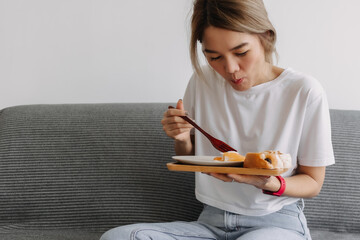 Asian woman concentrate on eating breakfast on the sofa. Concept of easy life.