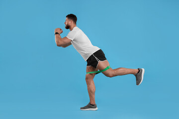 Fototapeta premium Young man exercising with elastic resistance band on light blue background