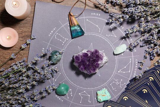 Astrology prediction. Zodiac wheel, gemstones, tarot cards and burning candles on wooden table, flat lay