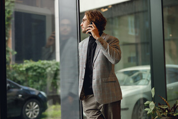 Handsome businessman in eyeglasses is talking phone standing in modern office near window