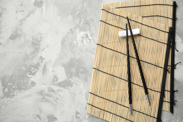 Bamboo mat with pair of black chopsticks and rest on grey textured table, top view. Space for text