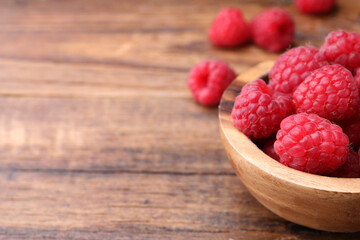 Tasty ripe raspberries in bowl on wooden table, closeup. Space for text