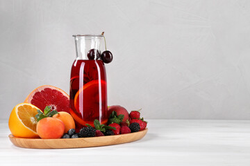Delicious refreshing sangria, fruits and berries on white wooden table, space for text