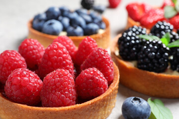 Tartlets with different fresh berries on light table, closeup. Delicious dessert