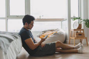 Lonely asian man using smartphone for social media alone in his apartment.