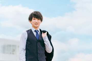 ジャケットを背負うベスト付きスーツを着た若いアジア人ビジネスマン
