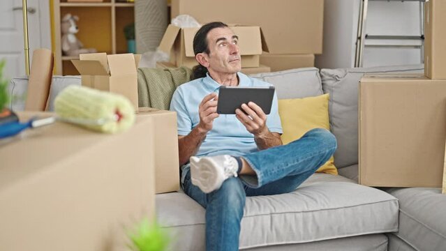 Middle age man having video call sitting on sofa at new home