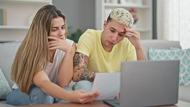 Beautiful couple using laptop reading document looking upset at home