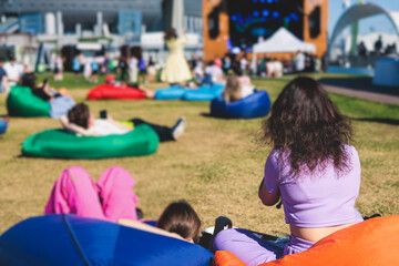 Crowded open air festival concert with musicians band on stage, rock show performance, with concert-goers attendees on beanbags, audience sitting on bean bag chair on a grass lawn on summer festival