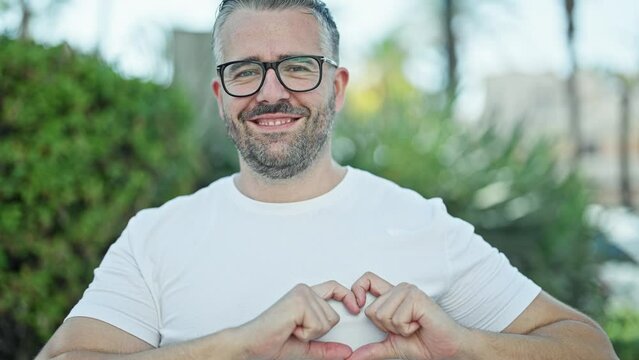 Grey-haired man smiling confident doing heart gesture with hands at park