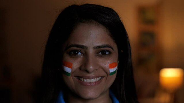 Young Indian female smiling towards the camera with a face painted in three colors of the Indian flag - female Indian cricket fan. A woman with a joyful smile - facing the camera  face painted with...