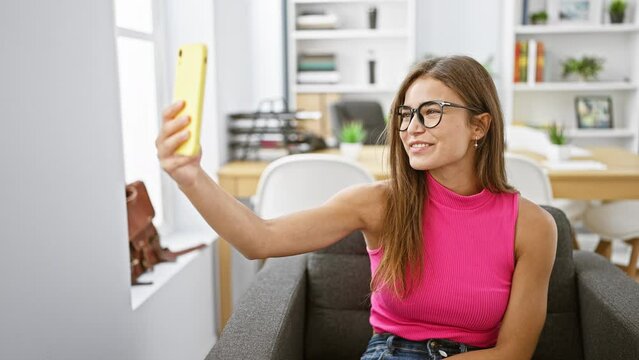 Happy days at work! radiant young hispanic businesswoman enjoys taking selfie in stylish office interior