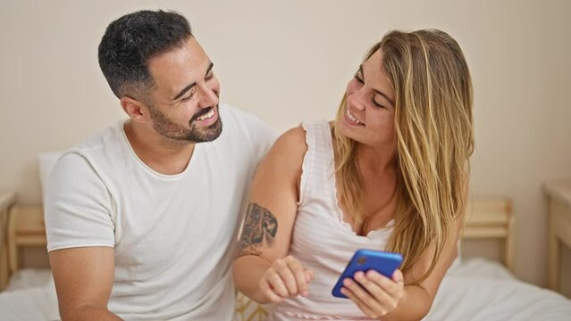 Man and woman couple sitting on bed using smartphone hugging each other at bedroom