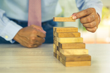 Hand placing wooden block tower stack in pyramid stair step with caution to prevent collapse or...