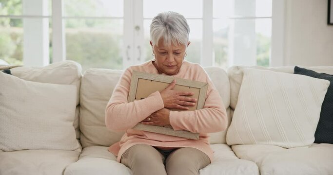 Depression, grief and senior woman on a sofa with photo album and ghost at home. Death, angel and elderly female widow hugging book past memories in living room sad, broken heart or mourning in house
