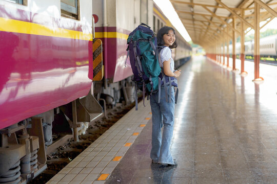 Young Asian woman traveler with a backpack on the railway, Backpack and hat at the train station with a traveler, Travel concept. Woman traveler tourist walking at a train station.