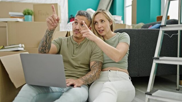 Man and woman couple using laptop looking around at new home