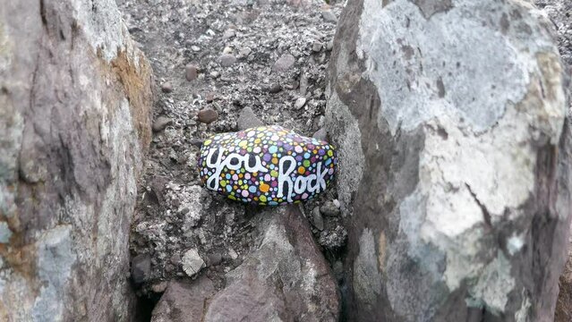 Kindness rock with uplifting message hidden between larger rocks