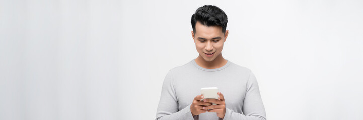 Handsome young man using his phone with smile while standing against white background.