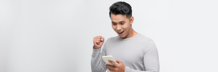A happy young man holding mobile phone and celebrating success isolated over white background