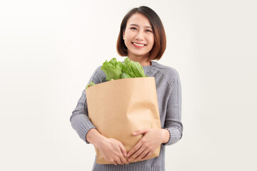Young asian woman smiles embraces paper bag with fresh products returns from supermarket