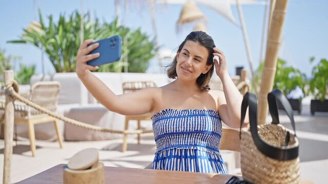 Young hispanic woman taking a selfie picture sitting on the table at sunny restaurant terrace
