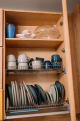 Fototapeta na wymiar The dishes are dried on a shelf in the kitchen cabinet. Plates and cups on the dryer. Plates and cups from ikea. The dining set is on the shelves