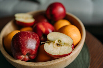 Fresh apples and oranges in a wooden plate. Some of the apples are cut into halves. Apples are ripe and red
