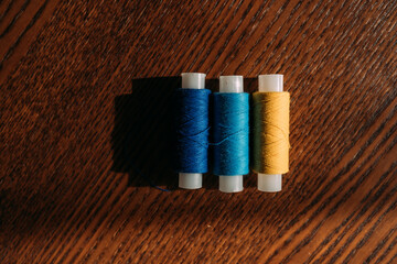 Eleven multicolored spools of thread lie in a row on a wooden table. Preparation for sewing. Rolls...