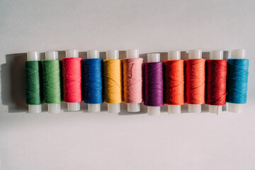Eleven multicolored spools of thread lie in a row on a white table. Preparation for sewing. Rolls of threads of different colors. a set of cotton threads, a set of bobbins. 