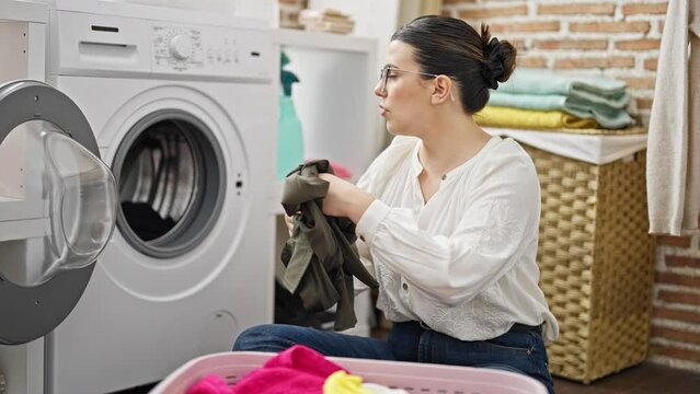 Young beautiful hispanic woman looking at instructions of washing machine at laundry room