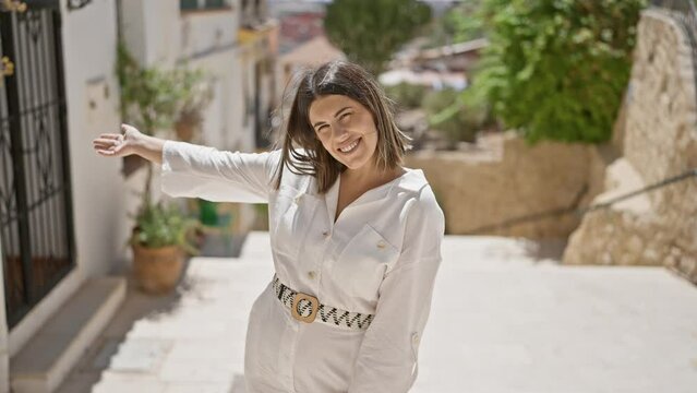 Young beautiful hispanic woman standing smiling showing the place at typical spanish old town