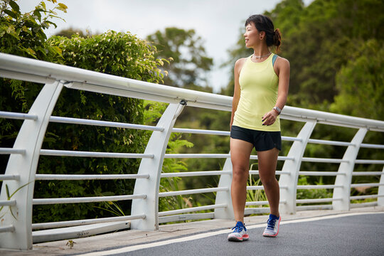 young asian woman jogger walking outdoors in park happy and smiling