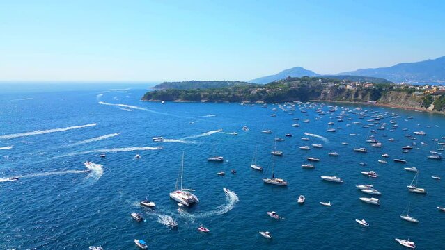 Aerial pullback from Panoramica sulla Corricella on Procida Island (Isola di Procida) with many white boats cruising the wavy blue Tyrrhenian Sea and leaving wakes amongst slopes and mountains