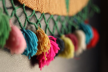 Rainbow colour Yarn Tassel Garland stitched to a piece of cloth in selective focus - obrazy, fototapety, plakaty