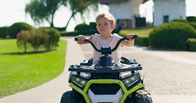A child driving a toy electric car in a park on a summer day