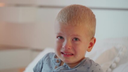 face of crying child little boy on the bed in bedroom at home