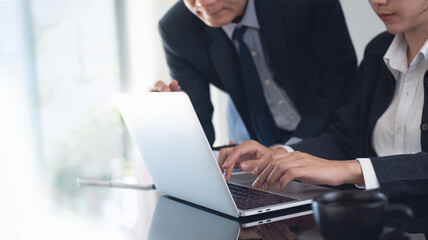 Two asian business persons working together. Businessman brainstorming, having a discussion with his colleague about work project, working on laptop computer at modern office. Business teamwork