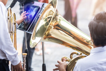 A musician's hand is touching the screen of a tablet placed on music stand with blurry brass...