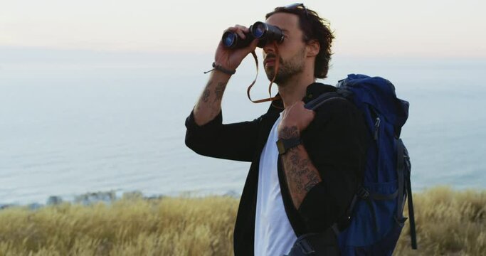 Nature, hiking and horizon, man with binoculars and backpack on hill for outdoor adventure. Mountain, ocean and hiker with view of water, trekking and thinking with freedom, peace and calm travel.