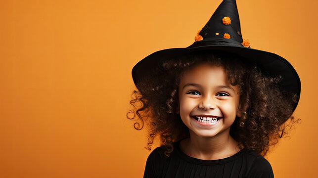 Portr&auml;t eines jungen lachenden M&auml;dchens f&uuml;r Halloween verkleidet. Mit schwarzem Hexenhut vor orange farbigen Hintergrund, mit Platz f&uuml;r Text