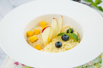 porridge with pieces of apple, mango, berries and mint in a white plate side view