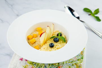 porridge with pieces of apple, mango, berries and mint in a white plate side view