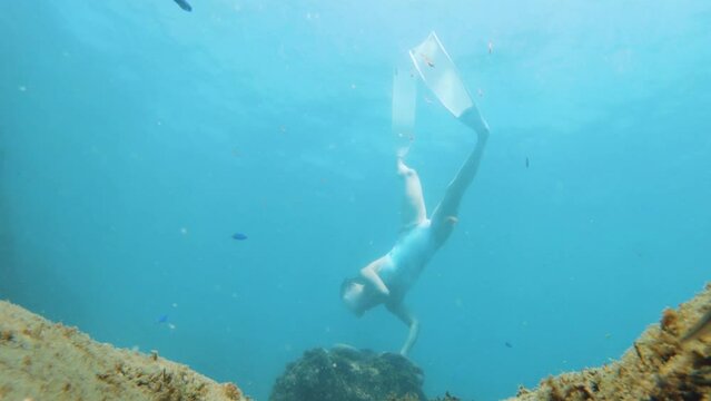 view of a young asian female free diver have fun ascending down into blue turquoise sea ripple bubble water grabbing holding weight rock stone to stabilize movement stand sit still at bottom seabed