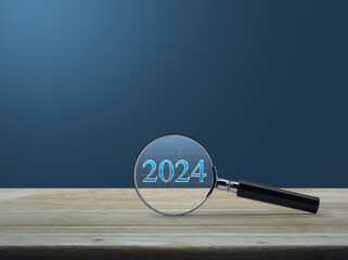 Magnifying glass with 2024 text and financial graph on wooden table over light blue wall, Business...