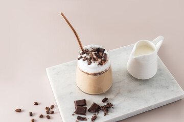 A large beautiful glass with a chic chocolate drink, a coffee or a cocktail with chocolate slices on a white marble podium, a pleasant romantic drink.