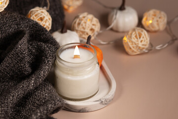 Fototapeta na wymiar Handmade coconut wax candle in a glass jar, autumn decorations with pumpkins, decor of cozy home interior