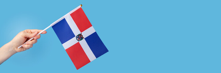 Dominican Republic flag in hand on a blue background, copy space, independence national day of...