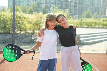 Kids and sports concept. Portrait of smiling girls posing outdoor on padel court with rackets and...