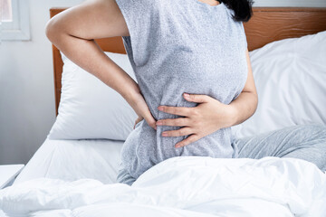 woman suffering from lower back pain , bad posture when sleeping in bed - obrazy, fototapety, plakaty